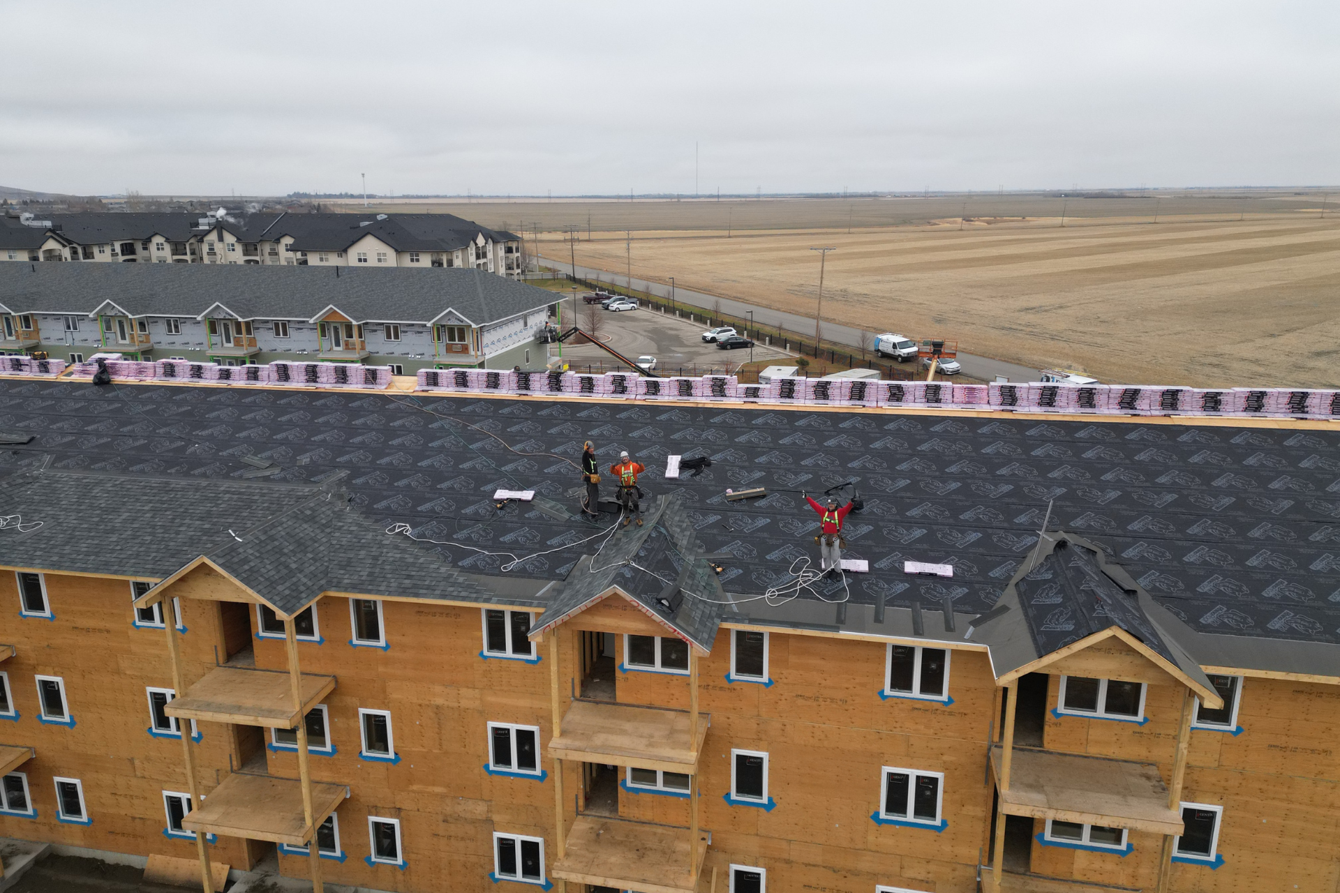 alt="Roofers working and waving from the top of a multi-unit building under construction, captured by drone in regina"